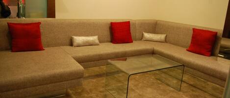 A modern living room with a beige sectional sofa, two red and two white cushions, and a glass coffee table.