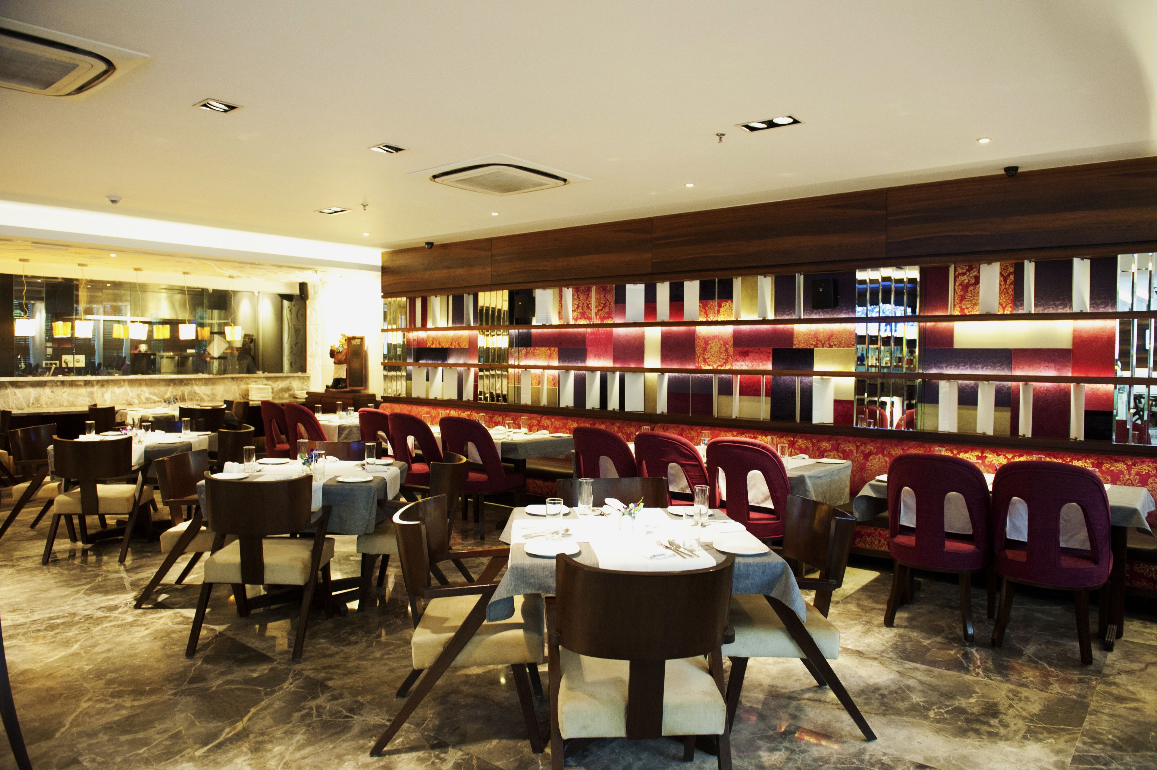 A restaurant with multiple tables and chairs, a bar area with a colorful wall, and a polished marble floor.