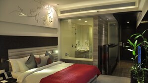 A modern hotel room with a large bed, a glass-enclosed shower, and a view of the city. - Maya Hotel (Chandigarh)