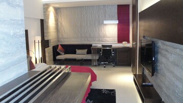 A modern hotel room with a sofa, a desk, and a TV.