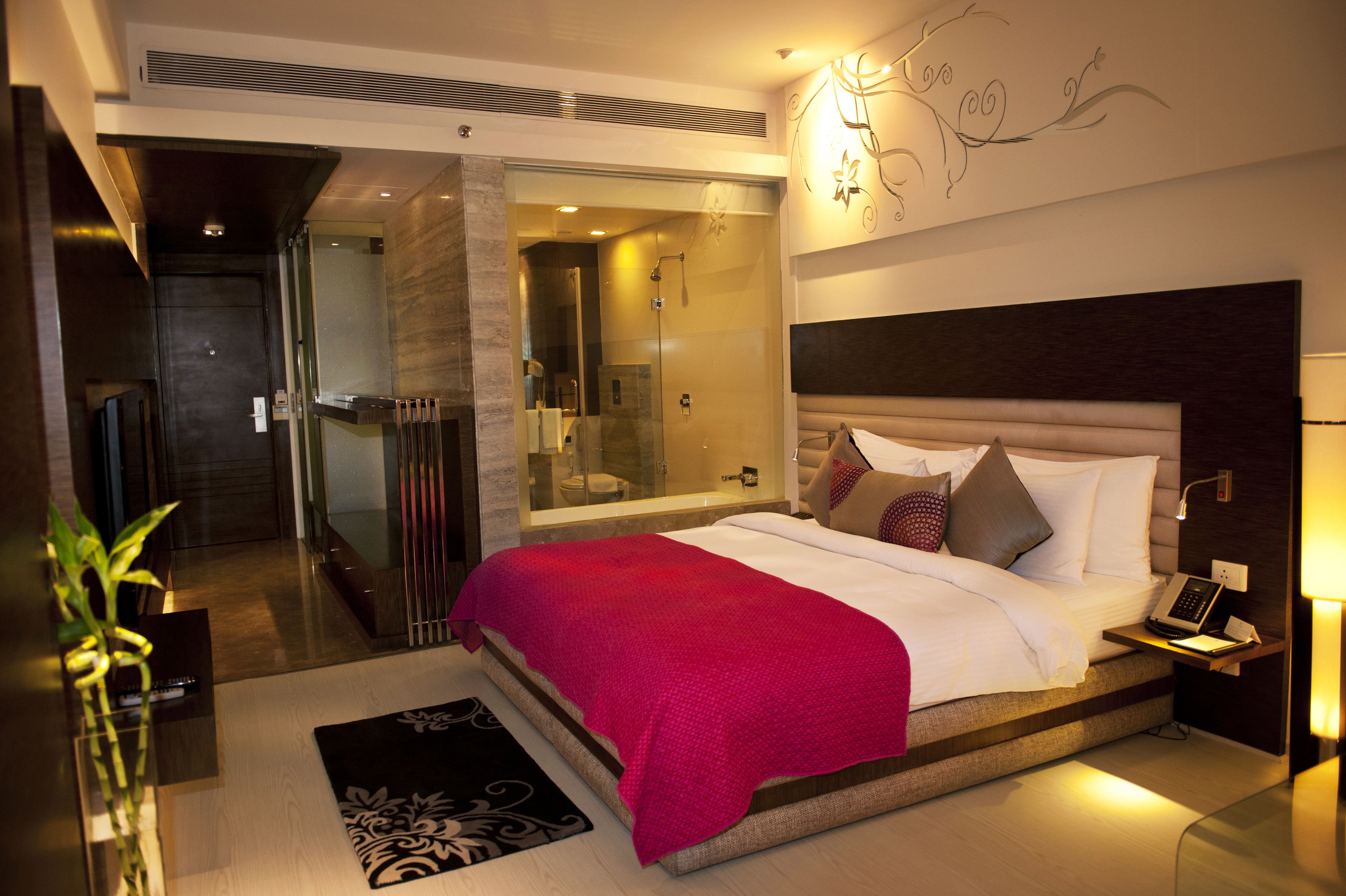 Une chambre d’hôtel moderne dotée d’un grand lit, d’une douche en verre, d’une table de chevet avec une lampe et d’un élément décoratif mural.