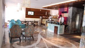 A hotel lobby with a reception desk, seating area with patterned chairs, a marble floor, and a television screen. - Maya Hotel (Chandigarh)