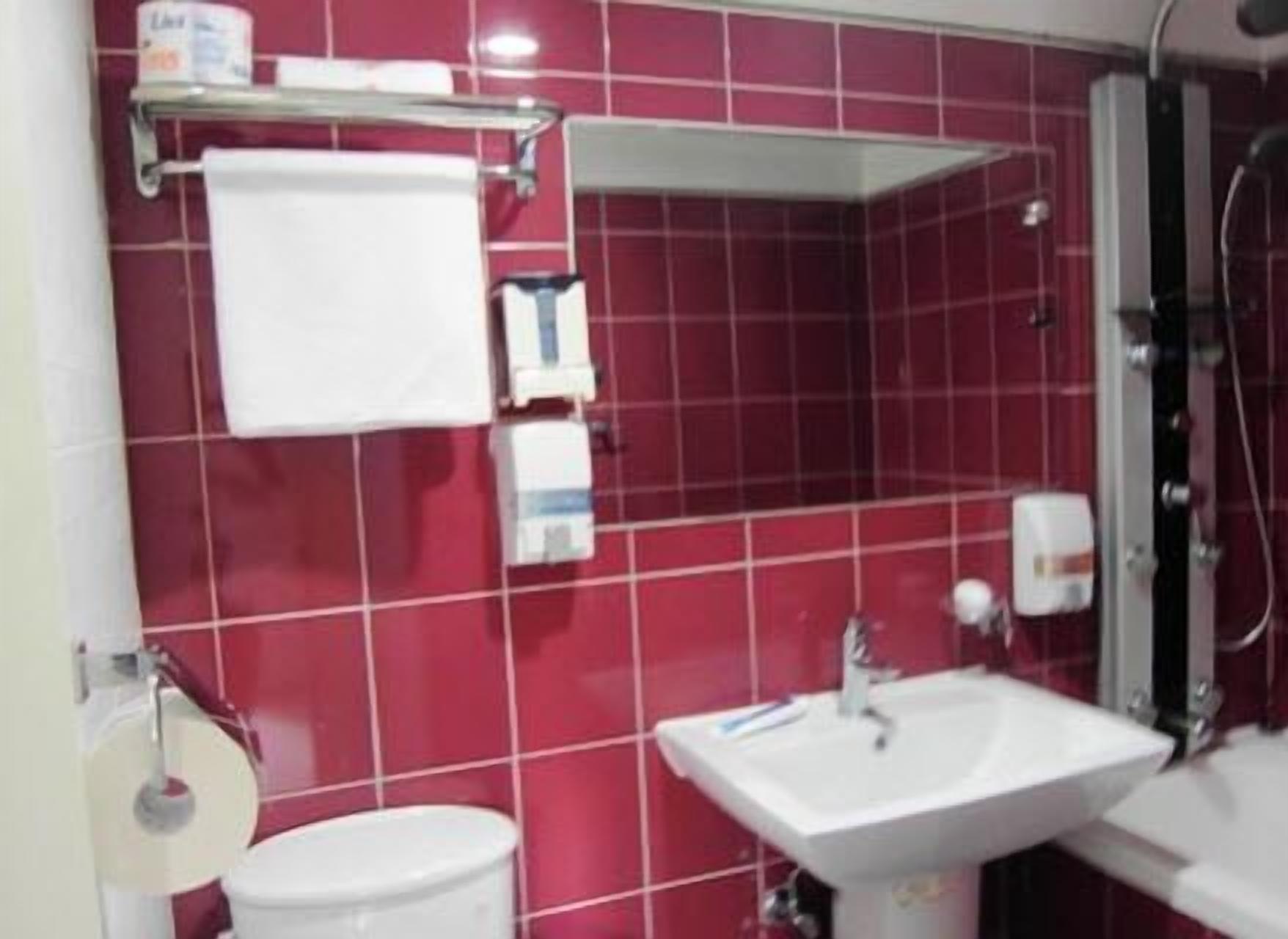 A bathroom with red tiles, a white sink, a toilet, and a shower area.