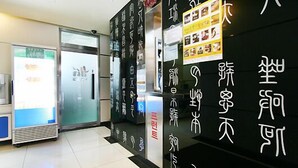 A reception area with a glass door, a vending machine, and a wall with text and images. - HIT Hotel (Seoul)