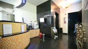 A hotel reception area with a tiled counter, a coffee machine, a fire extinguisher, and a digital screen. - HIT Hotel (Seoul)