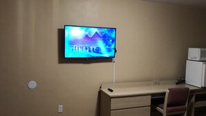 A room with a mounted TV displaying a blue landscape, a desk with a chair, and a microwave on a cabinet. - El Rey Motel (Globe)