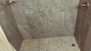 A shower area with tiled walls and floor, a drain, and a metallic door handle. - El Rey Motel (Globe)
