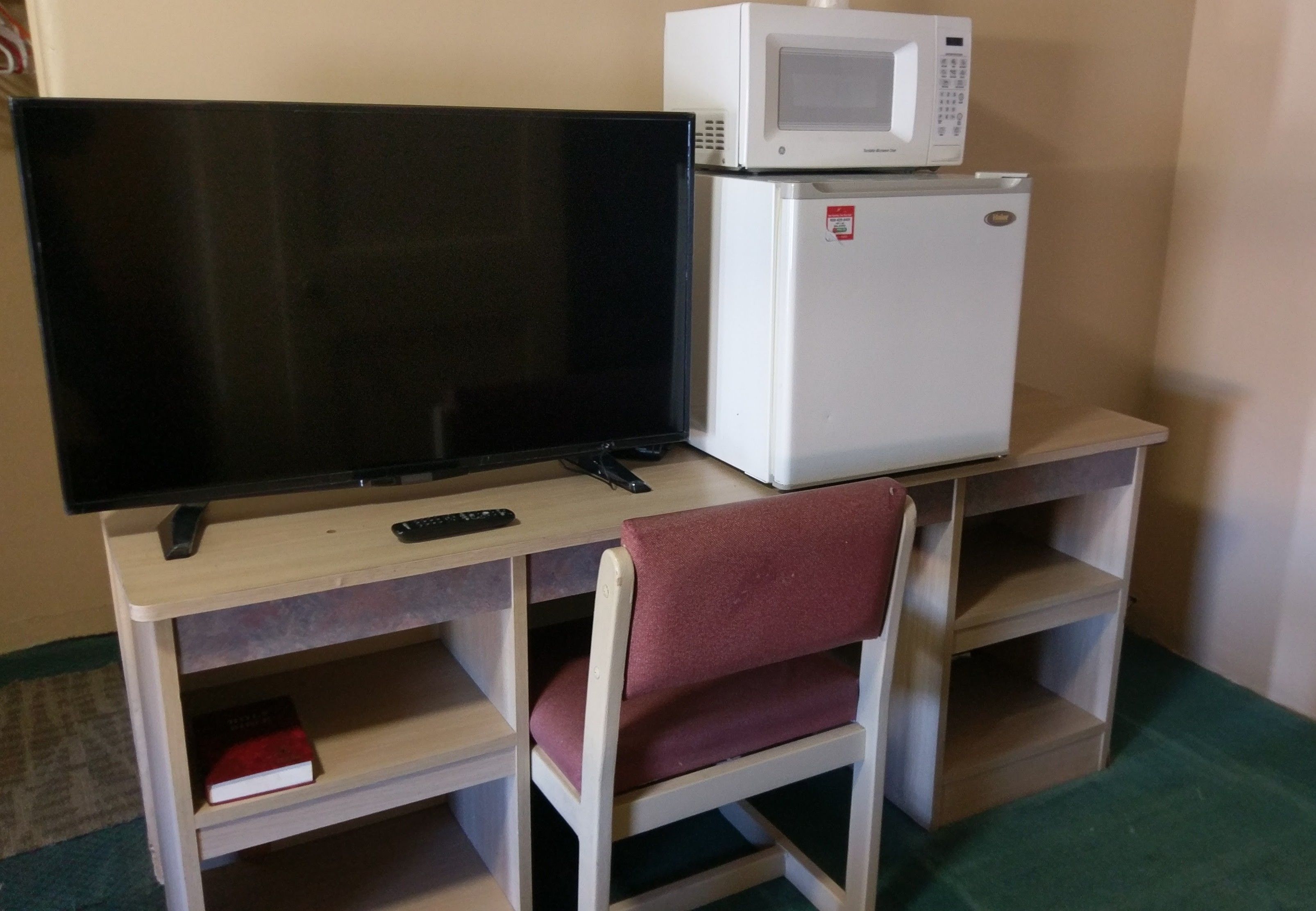 Una habitación compacta con televisión, microondas y un pequeño refrigerador sobre un escritorio de madera.
