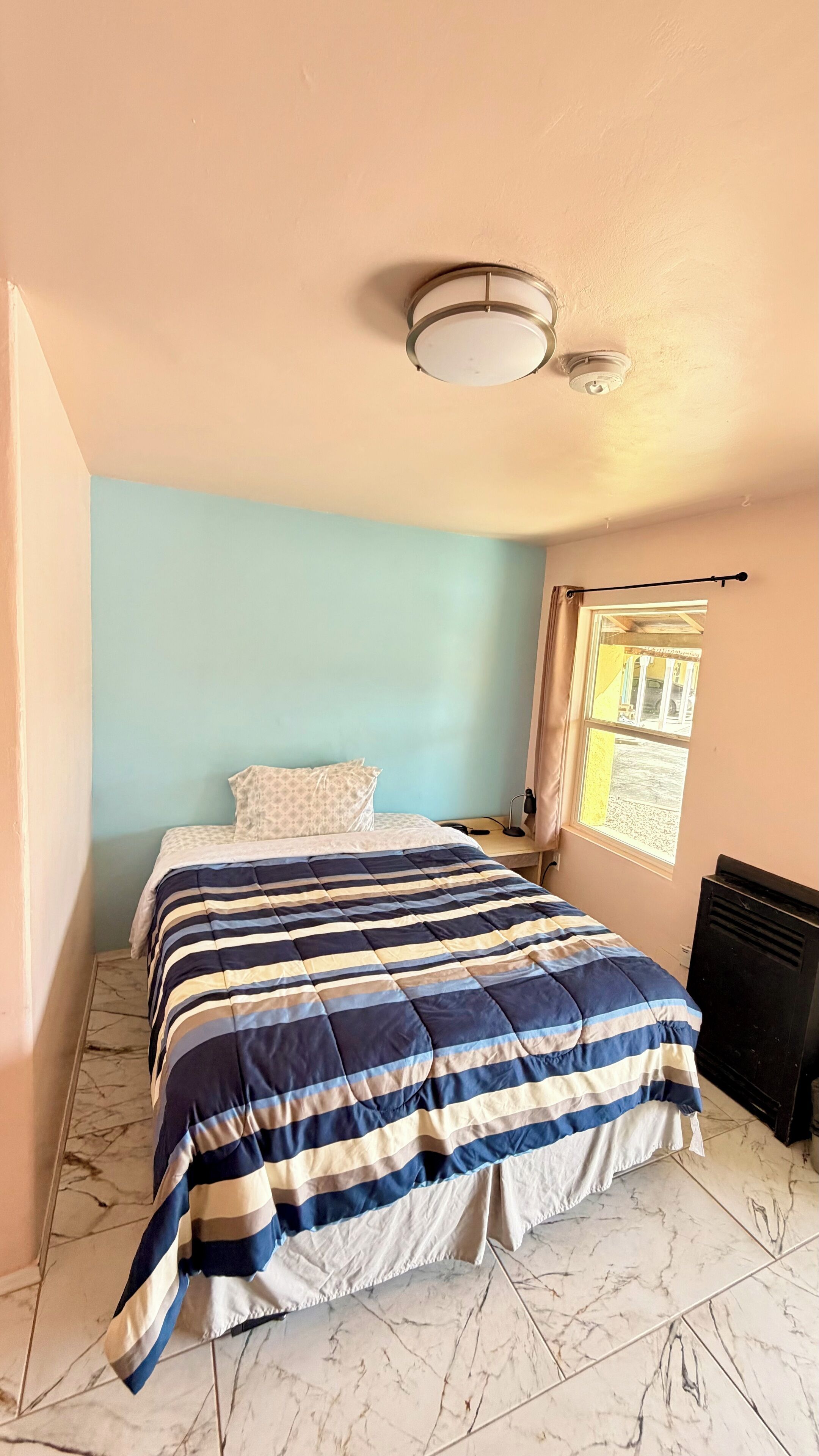 Een slaapkamer met een bed, een raam met gordijnen, een plafondlamp en een radiator.