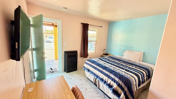 A bedroom with a bed, a desk, a television, and a door leading outside. - El Rey Motel (Globe)