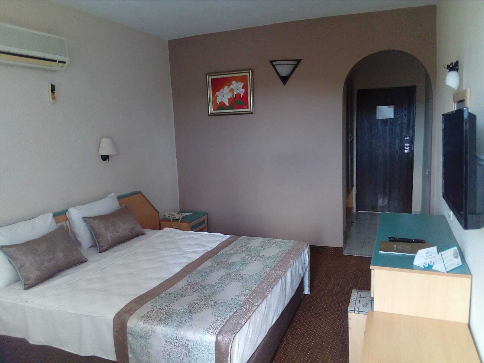 Une chambre d’hôtel avec un lit, un bureau avec un ordinateur, une télévision, un climatiseur, une lampe et un tableau au mur.