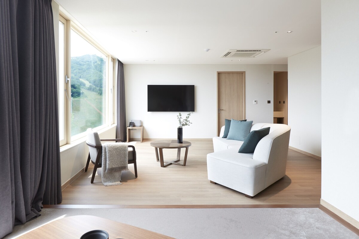 A modern living room with a white sofa, a small round table, and a TV mounted on the wall.