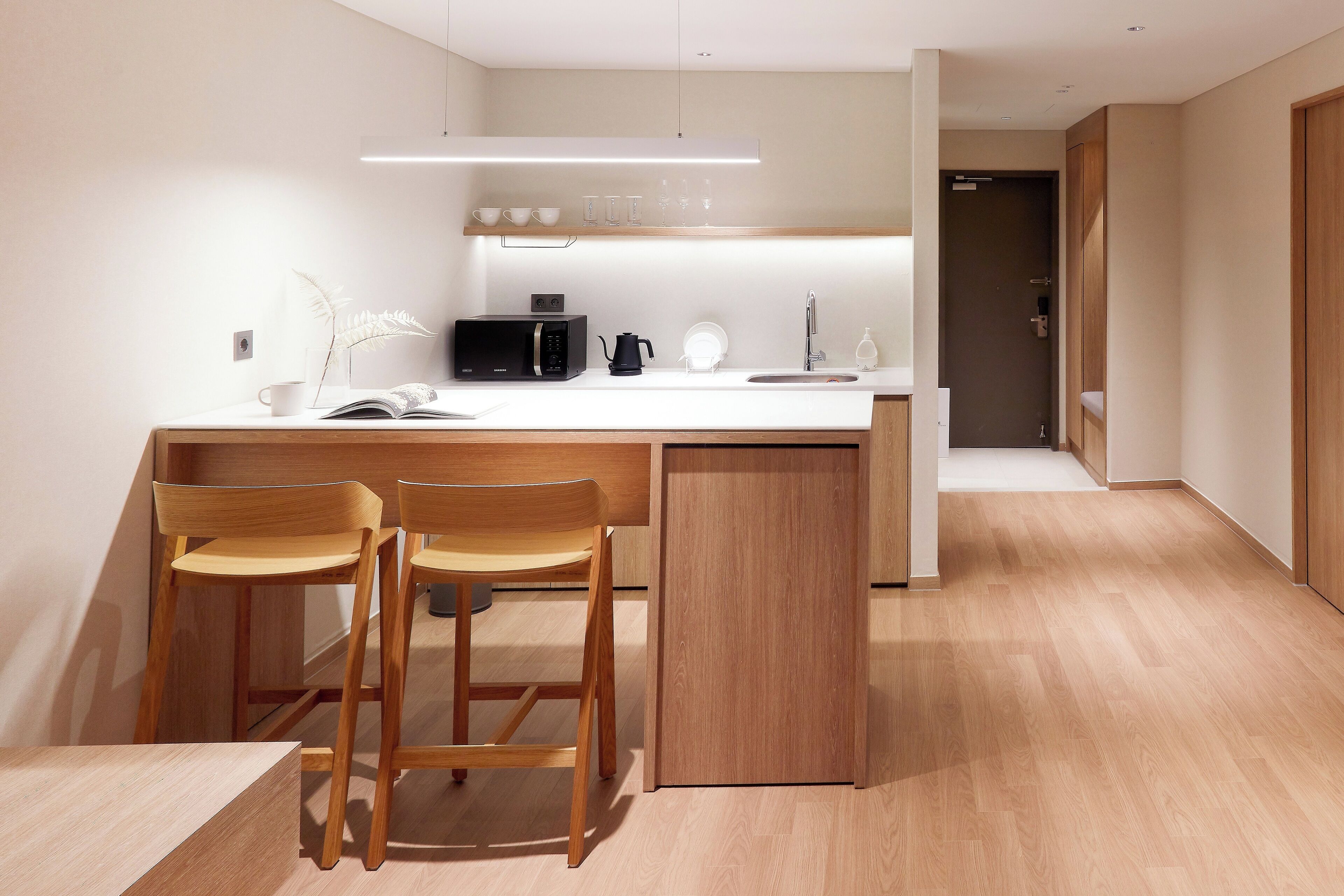 A modern kitchen with a central island, two wooden bar stools, a microwave, a coffee maker, and a sink.