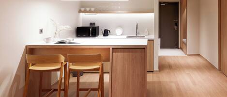A modern kitchen with a central island, two wooden bar stools, a microwave, a coffee maker, and a sink.