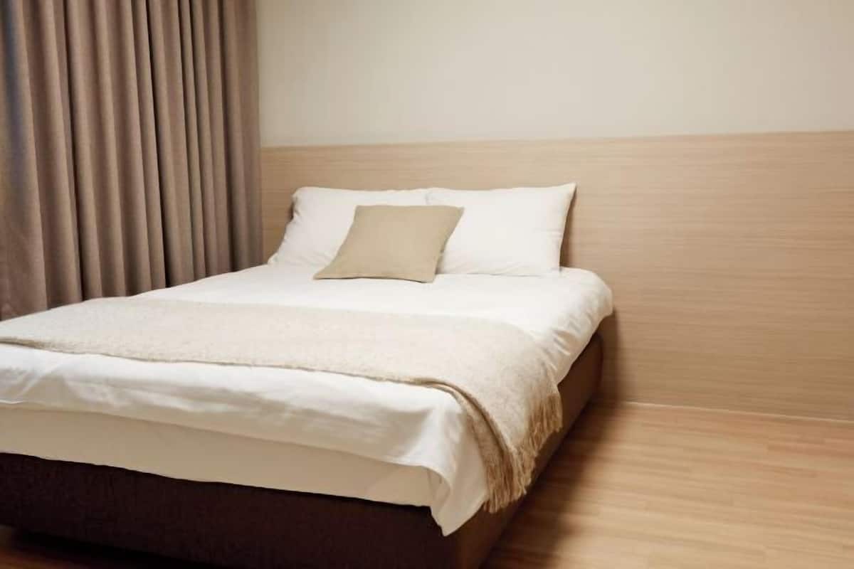 Ein ordentlich bezogenes Bett mit Kopfteil, einem beigen Kopfkissen und einer weißen Decke.