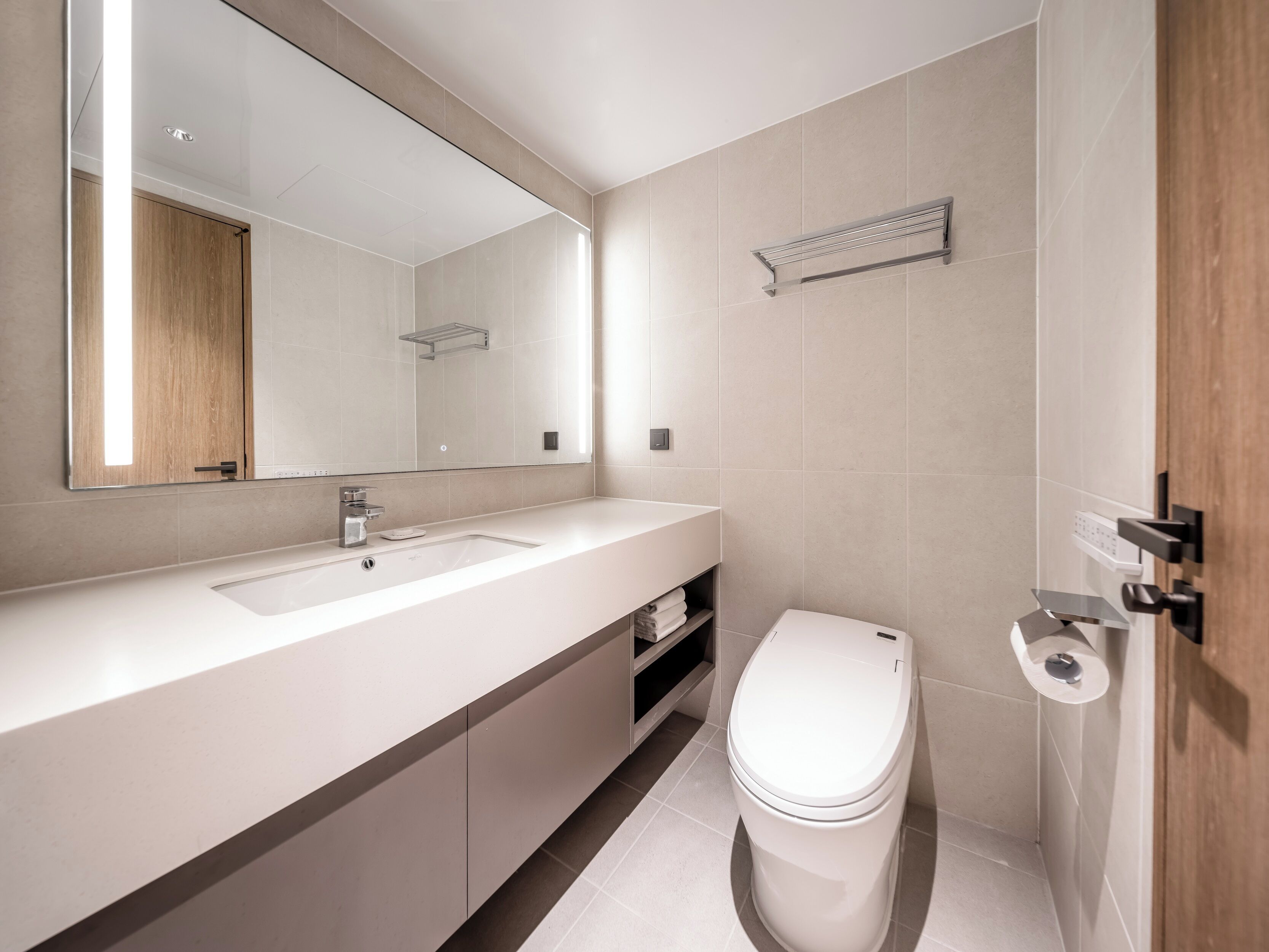 A modern bathroom with a large mirror, two sinks, a toilet, and a towel rack.