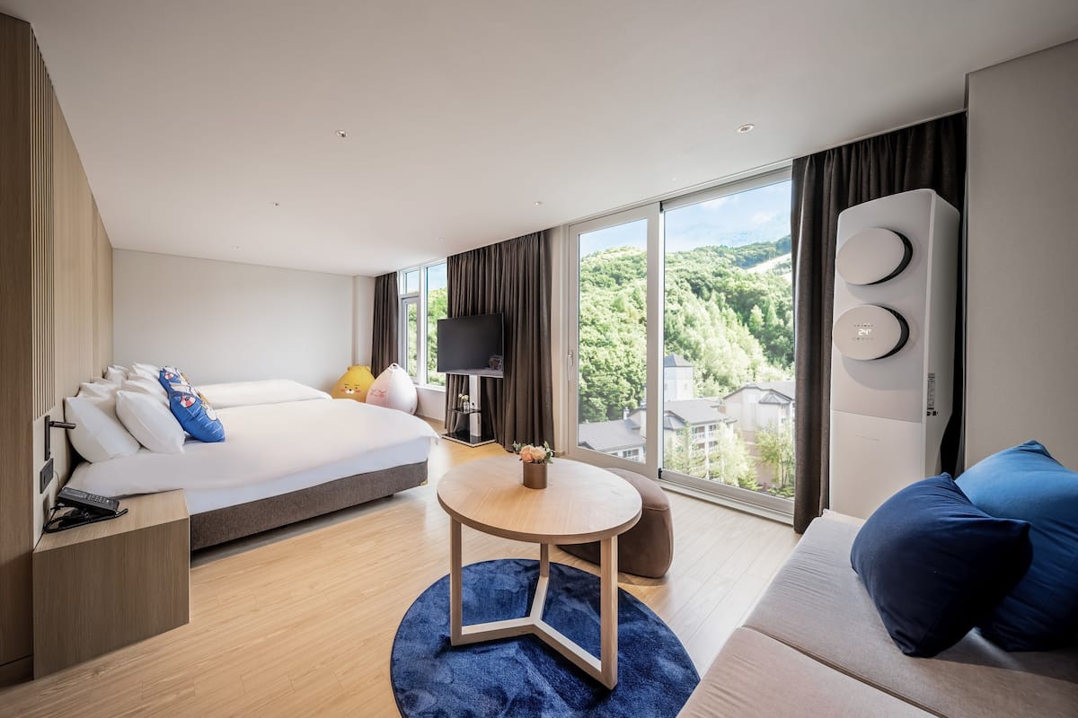 Ein modernes Hotelzimmer mit einem großen Bett, einer Couch, einem kleinen Tisch, einem Fernseher und Blick ins Freie.