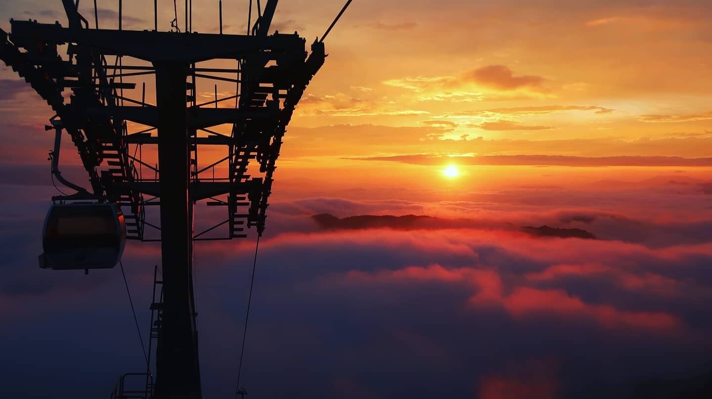 A high vantage point with a cable car system, overlooking a sunset over clouds.