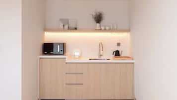 A modern kitchen with wooden cabinets, a microwave, a kettle, and a small shelf with decorative items.