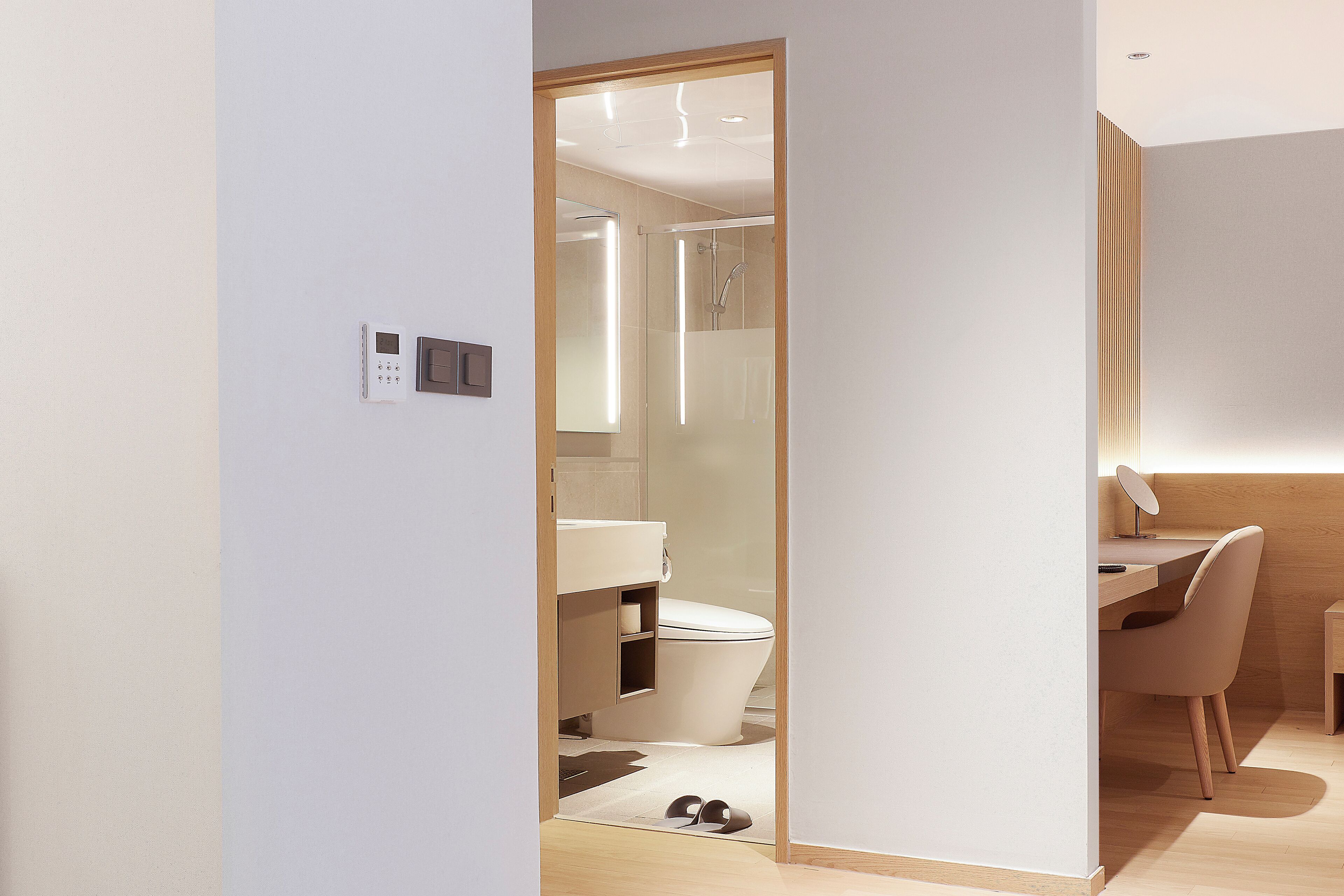 Un baño moderno con inodoro, ducha y una pequeña zona de escritorio con una silla y un pupitre.