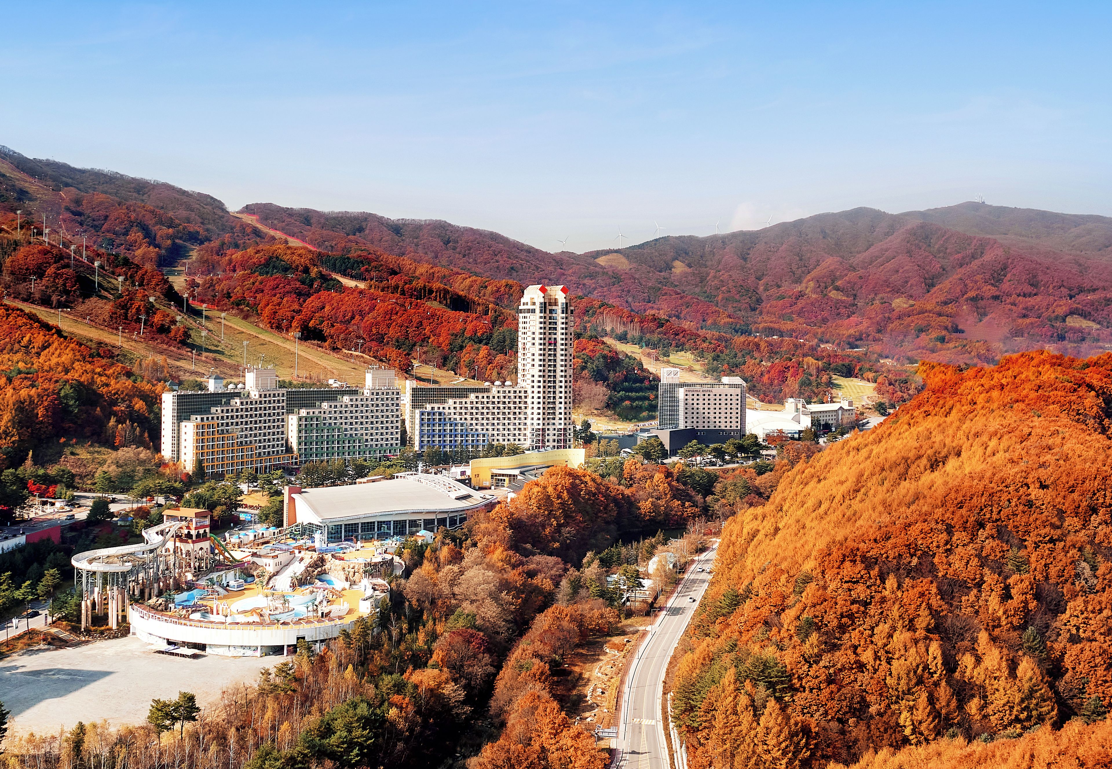 A hotel complex with multiple buildings, a parking area, and a view of the surrounding autumnal landscape.