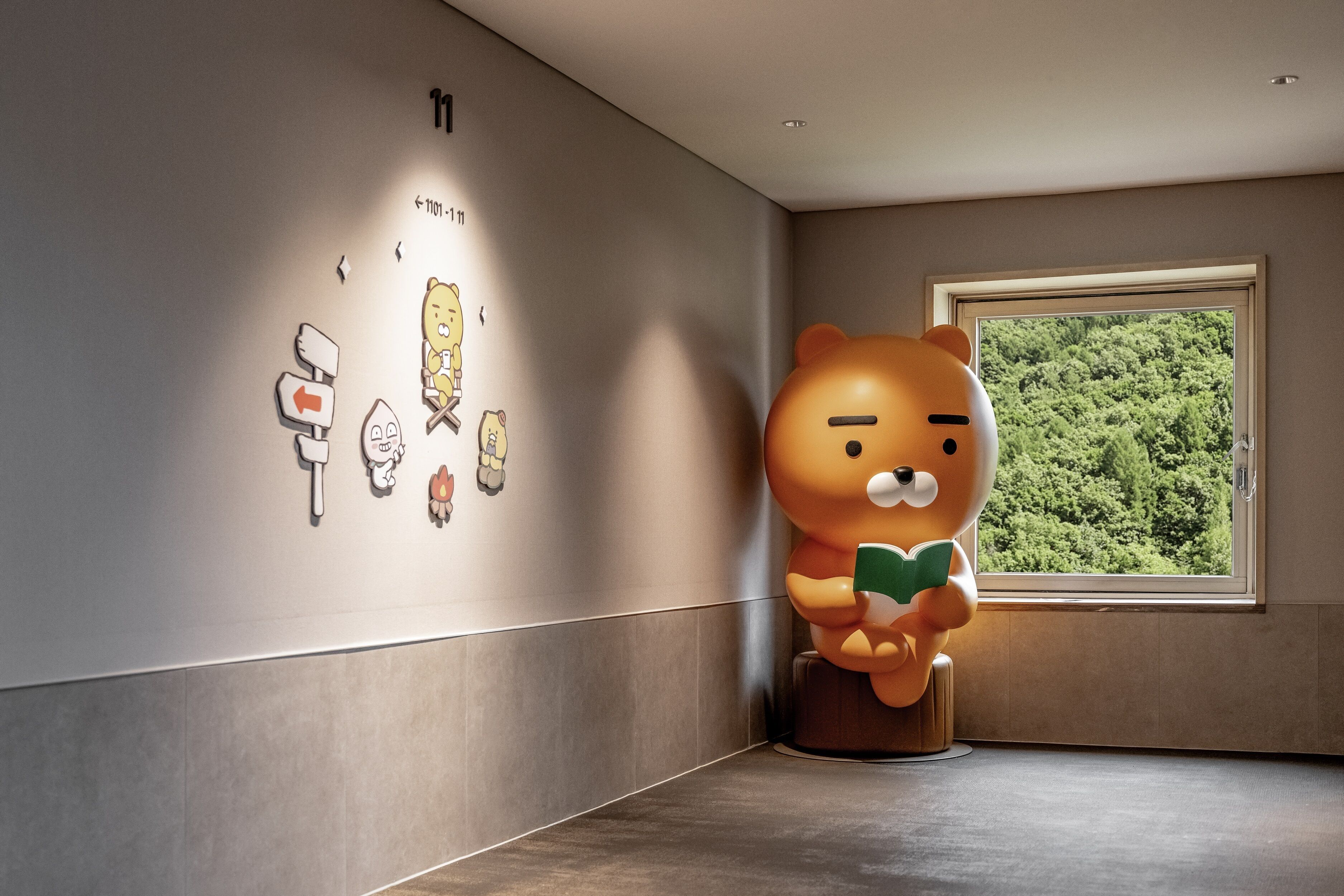 A bear statue reading a book in a room with a large window and wall art.