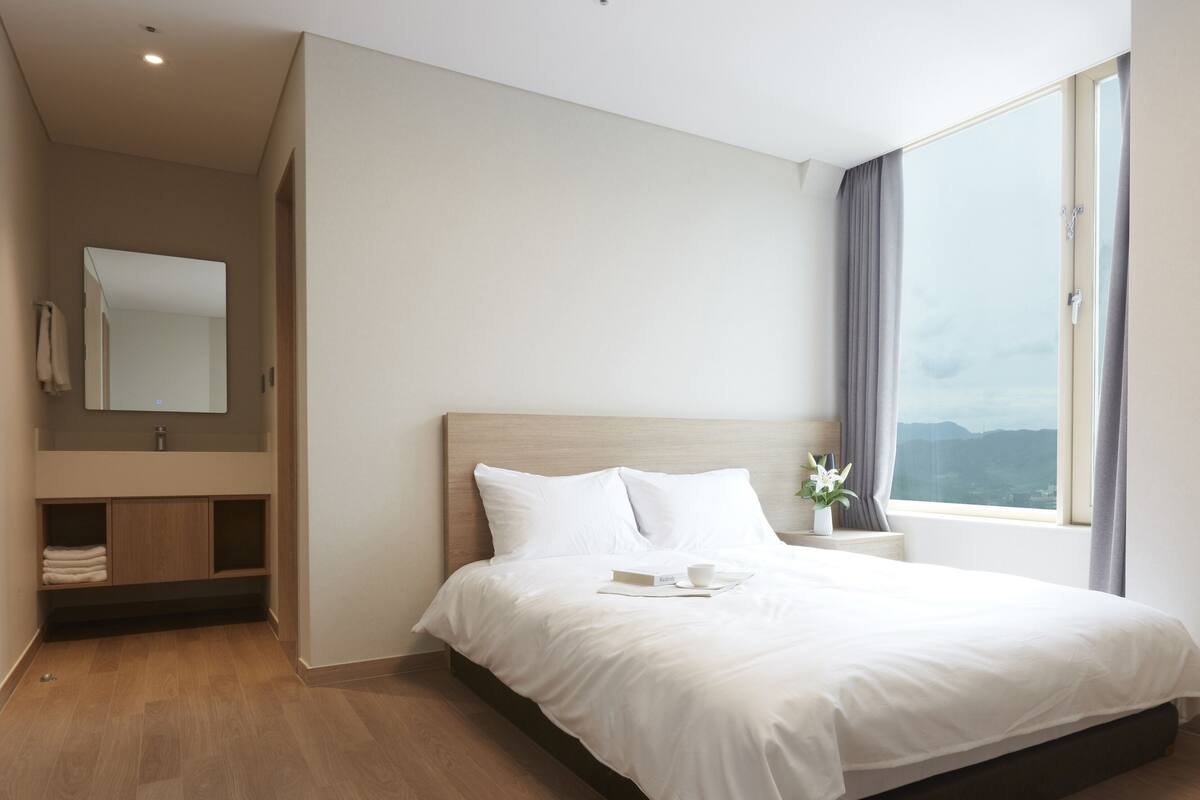 Ein modernes Hotelzimmer mit einem großen Bett, einem integrierten Schminktisch und einem Fenster mit Blick.