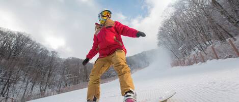 Una persona practicando snowboard en una ladera nevada, con árboles al fondo.