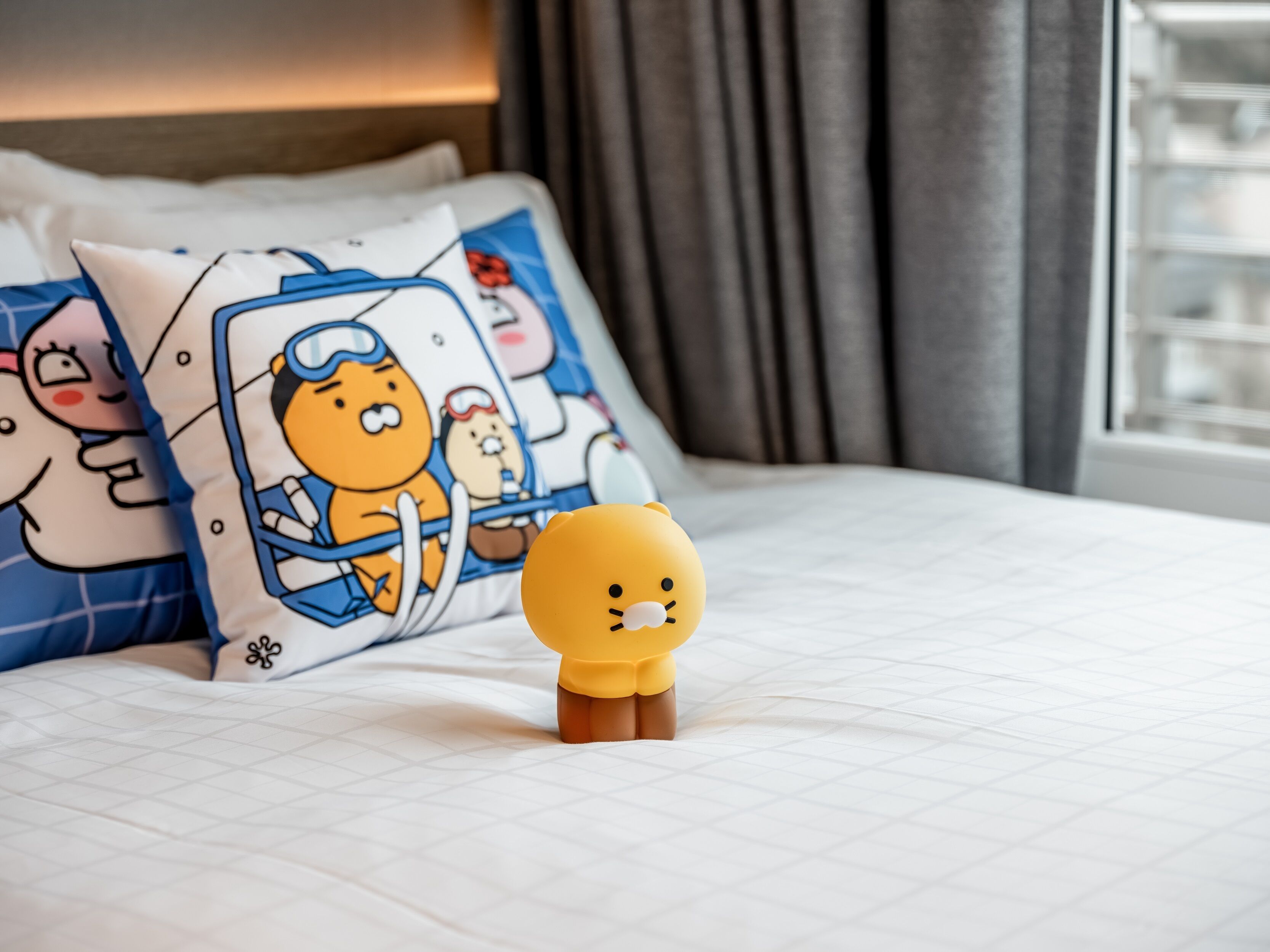 A bed with a white quilted cover, two pillows with cartoon characters, and a small yellow figurine on the bed.