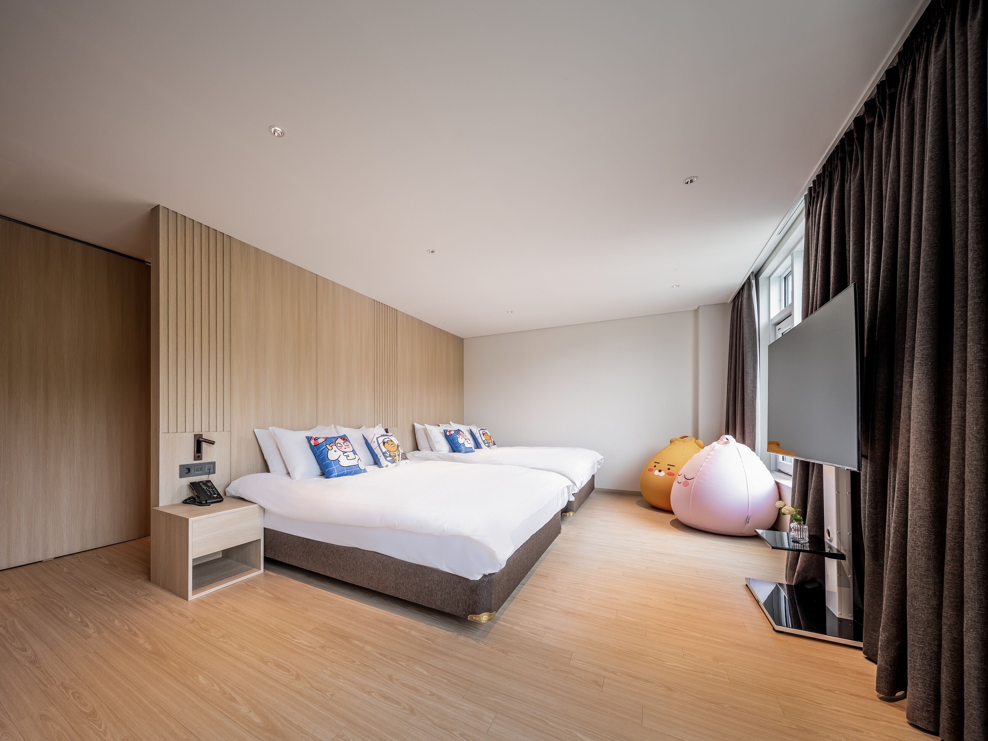 A modern hotel room with a large bed, bedside tables, a flat-screen TV, and a large window with curtains.