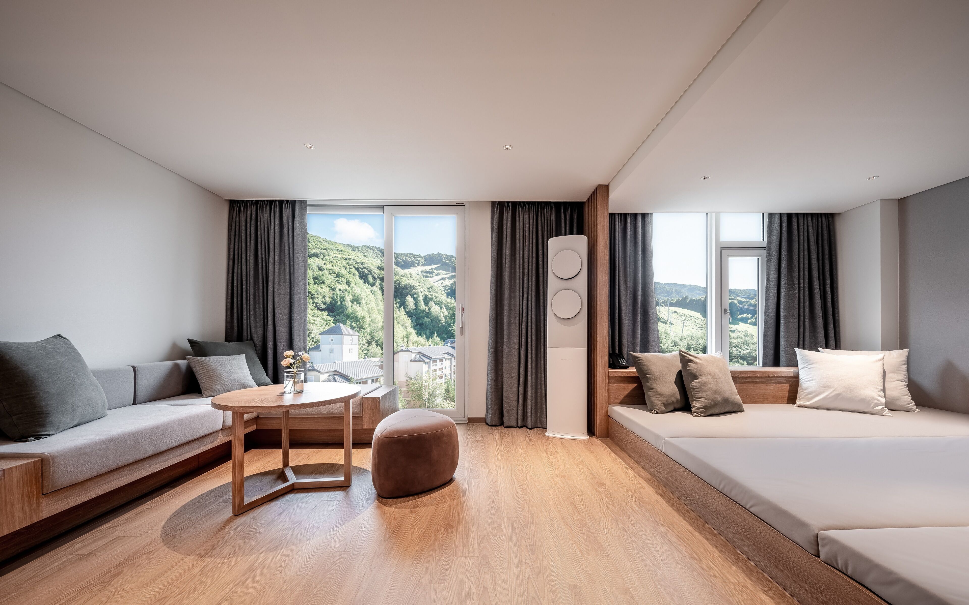 A modern hotel room with a sofa, a round table, and a view of a mountainous landscape.