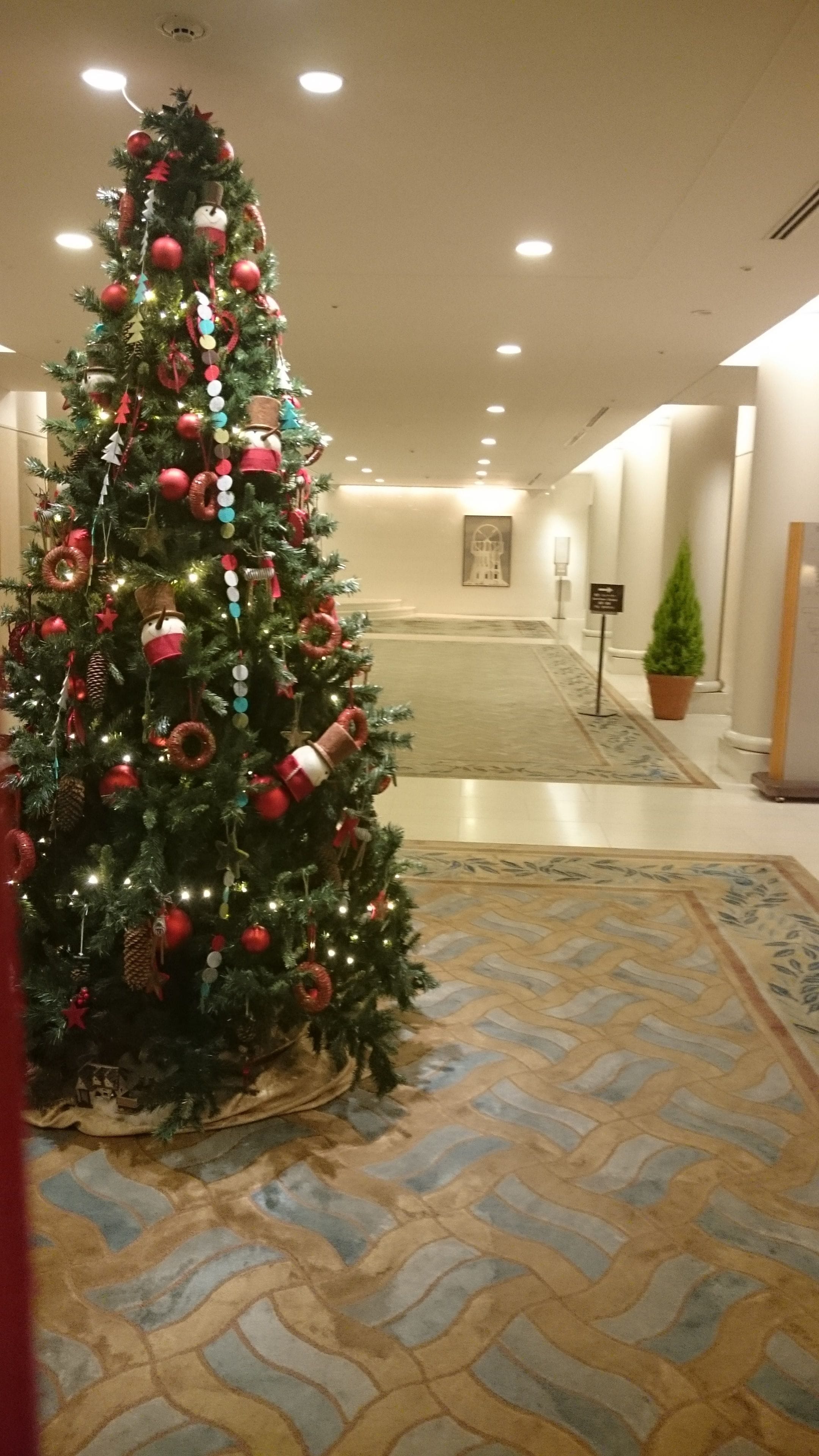 A Christmas tree in a hotel lobby with a patterned floor and a framed picture on the wall.