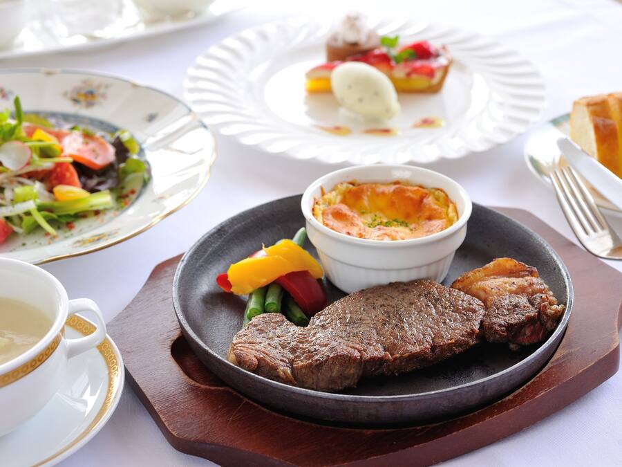 Una mesa de comedor con una variedad de platos, incluyendo un bistec, verduras y un tazón de sopa.