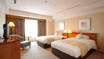 Quarto de hotel com duas camas, uma escrivaninha, uma cadeira e uma televisão.