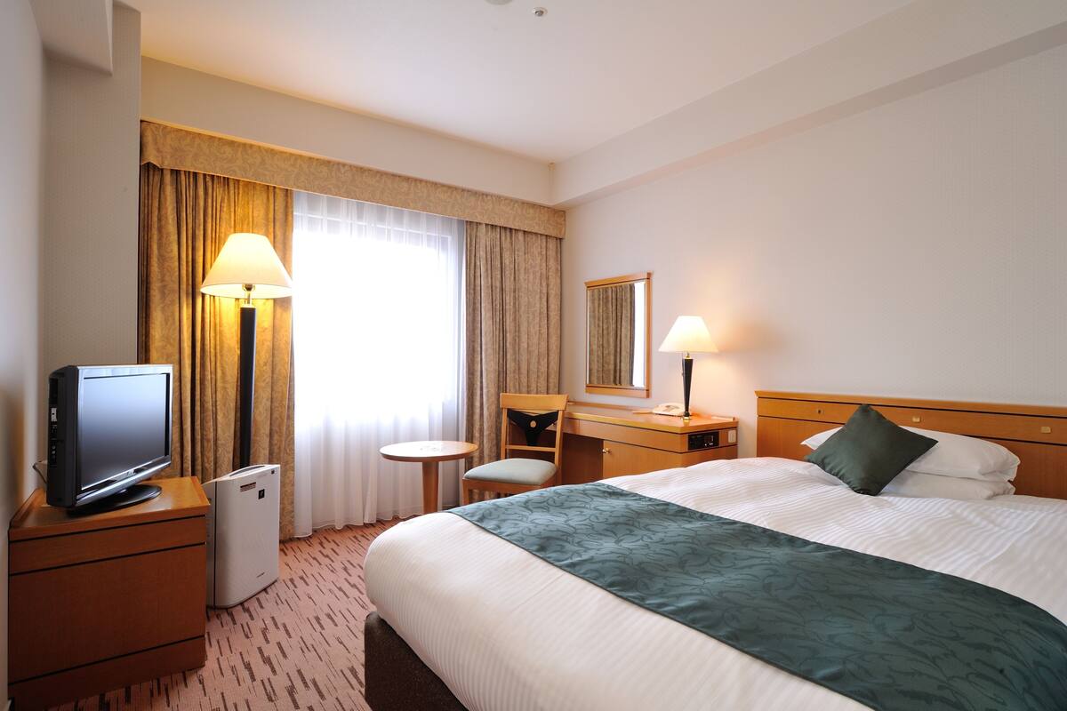 Une chambre d’hôtel comprenant un lit, un bureau avec une lampe, une chaise, une télévision et un mini-réfrigérateur.