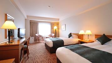 A hotel room with two beds, a desk with a lamp, a chair, a television, and a window with curtains.