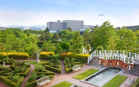 A landscaped garden with a pond, benches, and a white bridge.