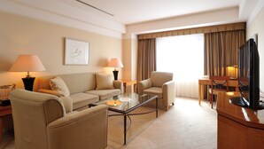 Ein Hotelzimmer mit einer Couch, Sesseln, einem Glastisch, einem Fernseher und einem Essbereich mit Tisch und Stühlen.