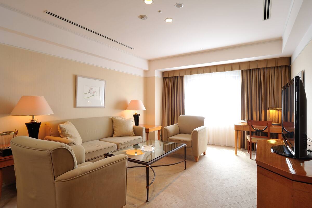 Une chambre d’hôtel comprenant un canapé, des fauteuils, une table basse en verre, un téléviseur et un coin repas avec une table et des chaises.