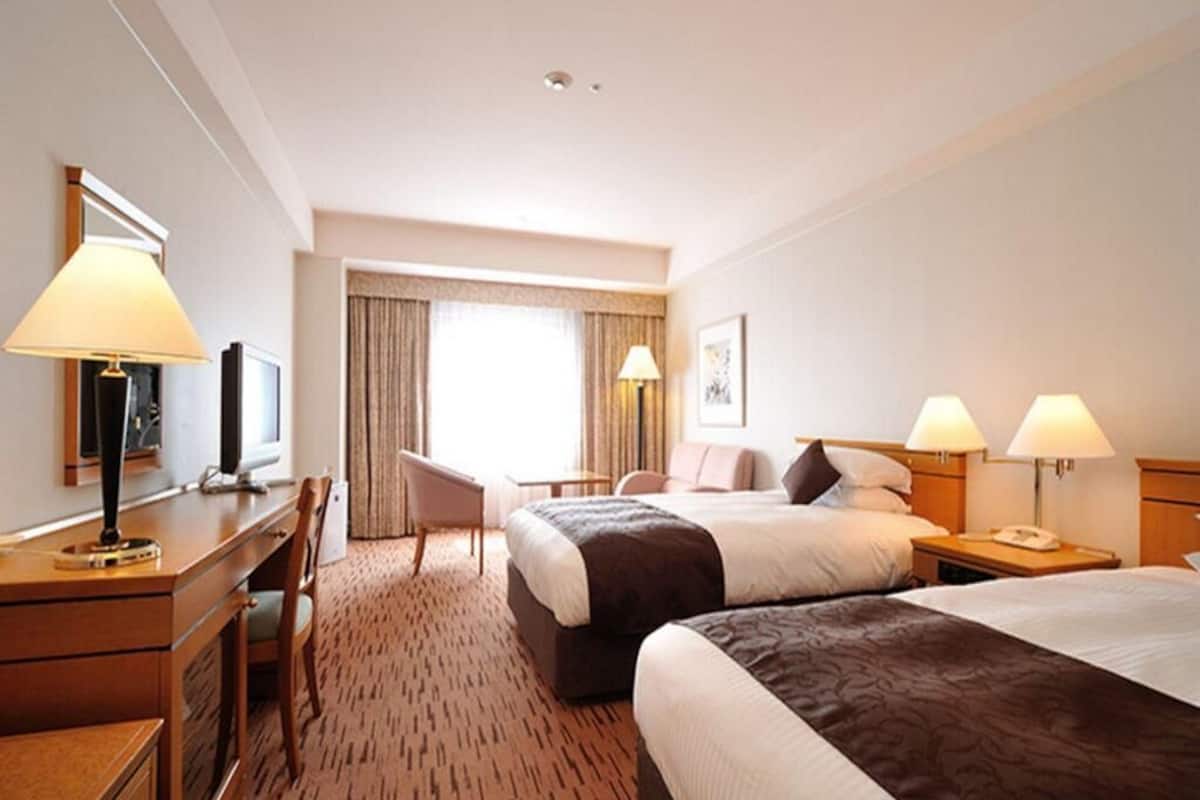 Une chambre d’hôtel avec deux lits, un bureau, une chaise, une télévision et une fenêtre avec des rideaux.