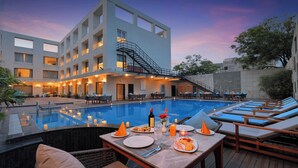 A poolside dining area with tables, chairs, and a pool. - The Retreat (Agra)