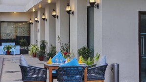 A poolside area with wicker chairs, a table set for dining, and a pool. - The Retreat (Agra)
