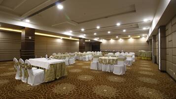Un amplio salón de banquetes bien iluminado con filas de mesas redondas cubiertas con manteles blancos y fajos verdes, dispuesto para un evento formal.