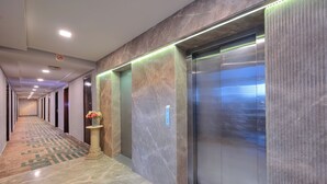 A long hallway with a patterned carpet, a column with flowers, and an elevator with a metallic finish. - The Retreat (Agra)