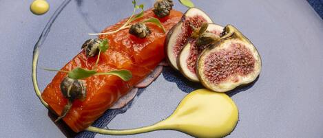 A dish with salmon, figs, and a yellow sauce on a blue plate.
