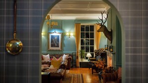 A cozy living room with a fireplace, a mounted deer head, and a large window with curtains. - Knipoch House Hotel (Oban)