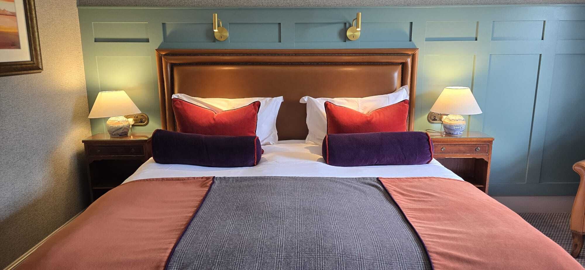 A hotel room with a large bed, two bedside tables, lamps, and a wooden headboard.