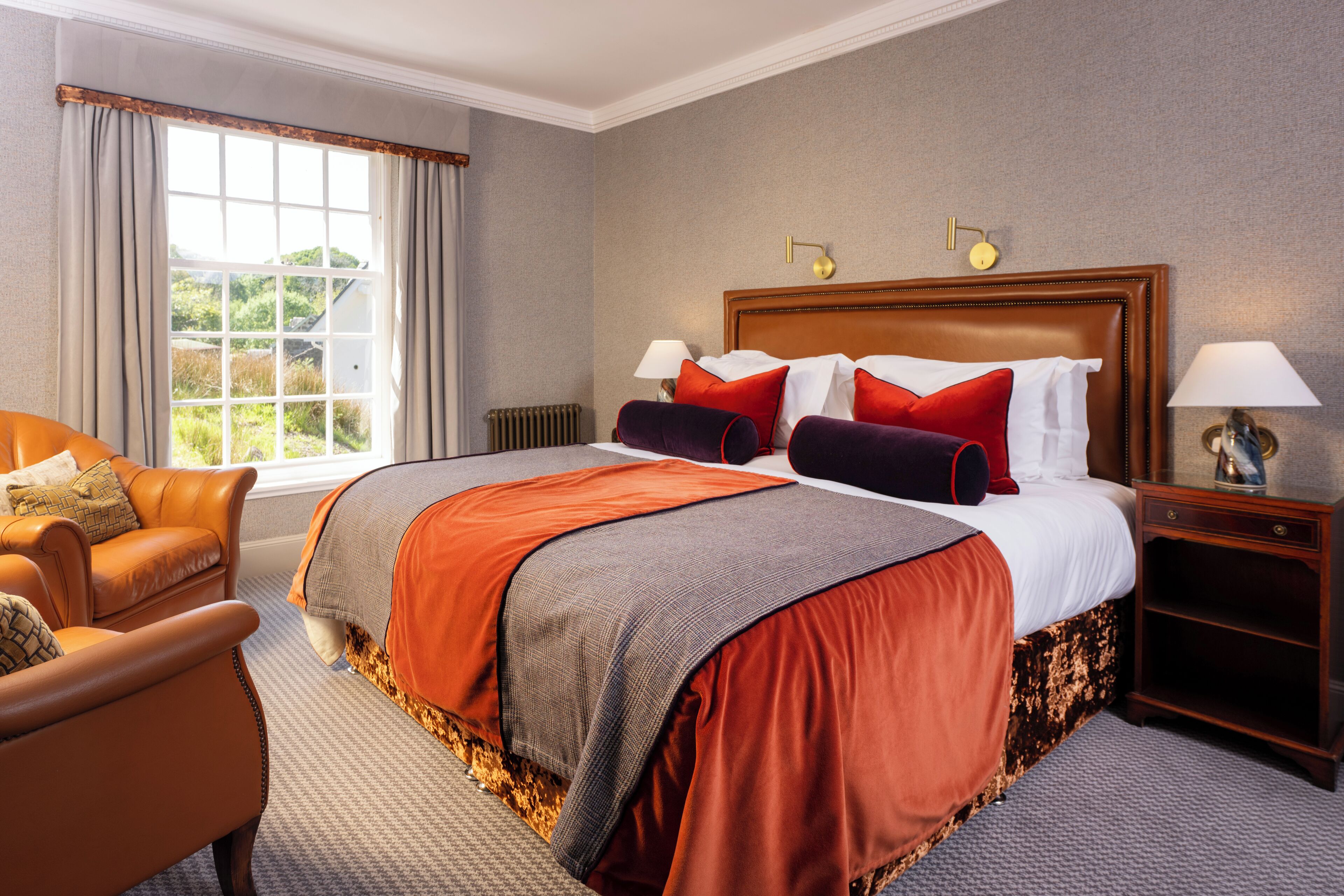 A hotel room with a large bed, two bedside tables, a window with curtains, a leather armchair, and a radiator.
