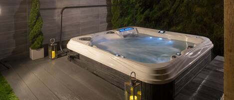 Een hottub met een houten terras, een plant in pot en twee lantaarns.