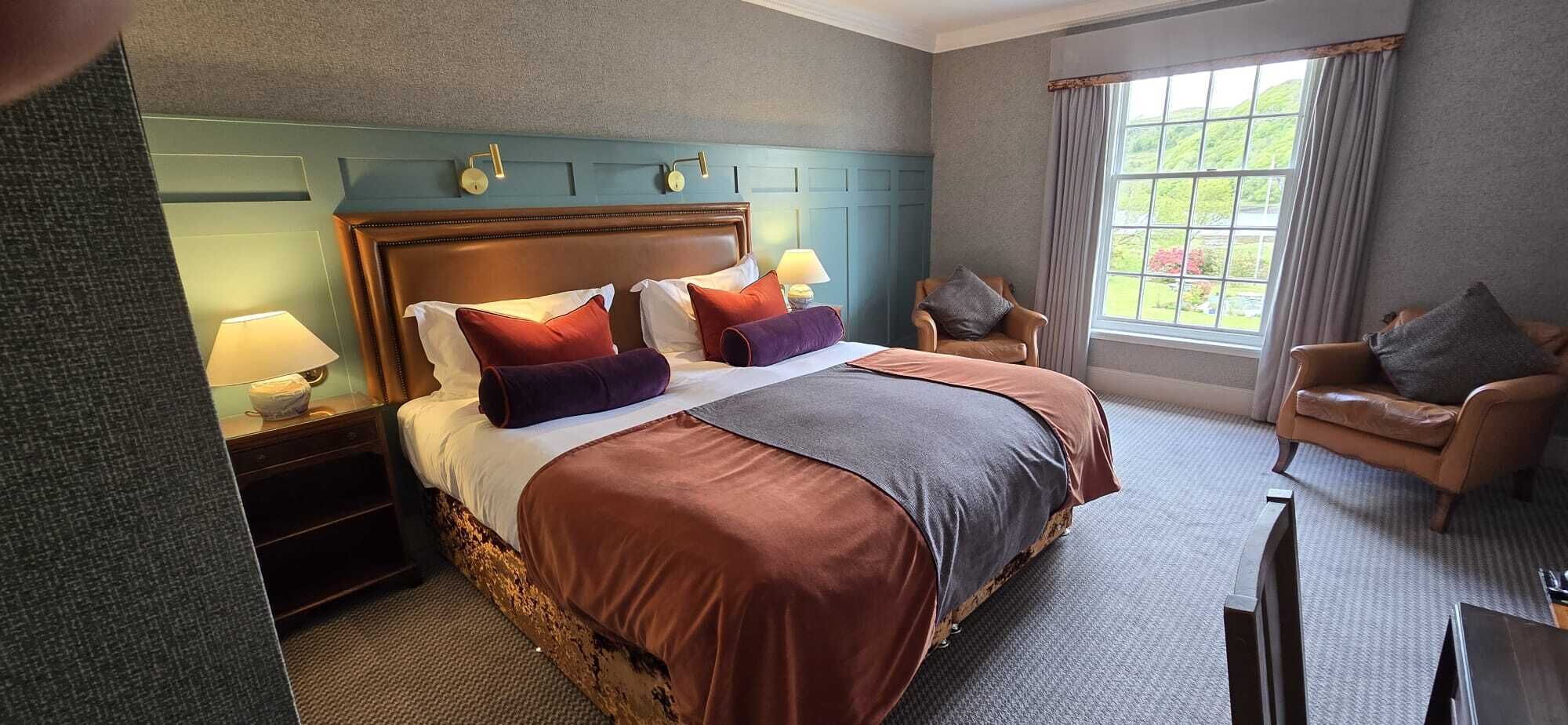 Ein Hotelzimmer mit einem großen Bett, einem Sessel, einem Schreibtisch und einem Fenster mit Blick.